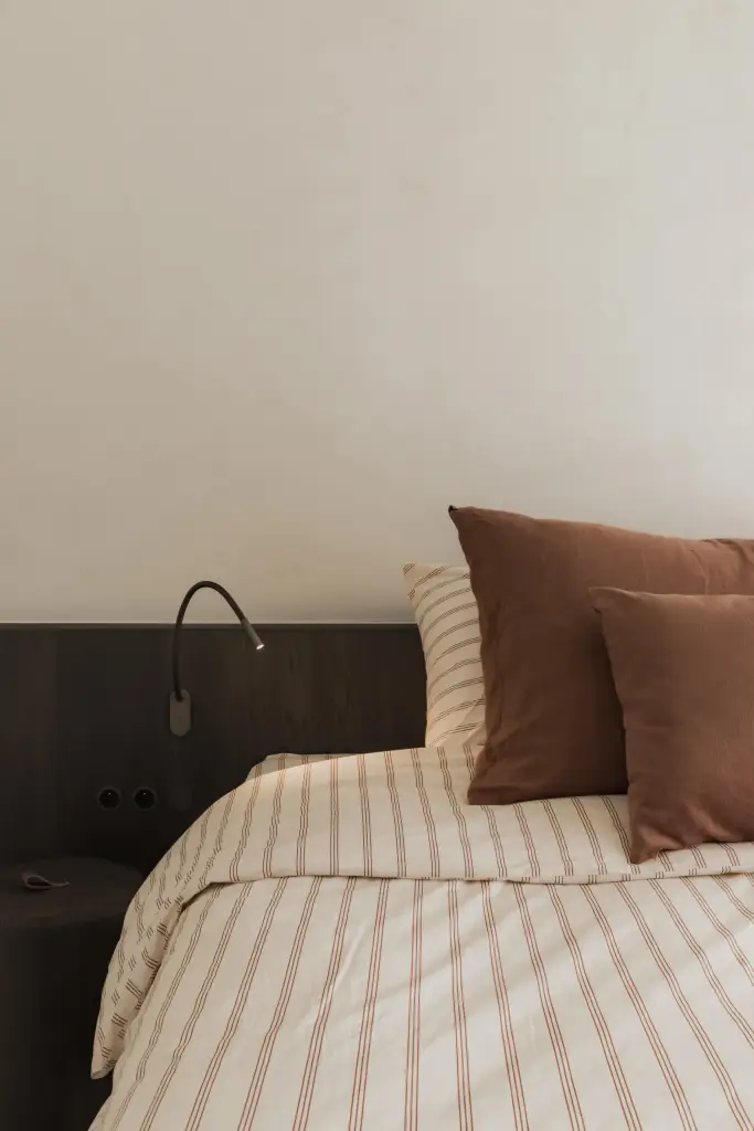 Bed met hoofdbord, leeslamp en terracotta kussens, Appartement in Nieuwpoort, interieur Laura Calleeuw