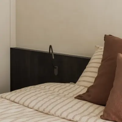 Bed met leeslamp en kussens naast een donker nachtkastje, Appartement in Nieuwpoort, interieur Laura Calleeuw