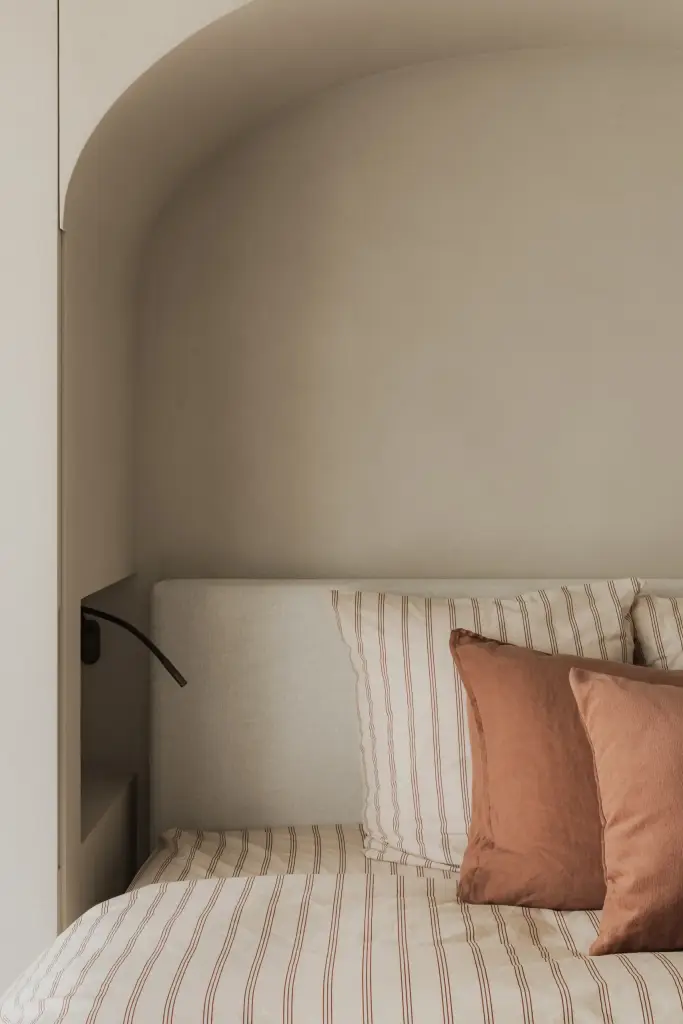 Het bed in de boogvormige nis met gestreept beddengoed en kussens, Appartement in Nieuwpoort, interieur Laura Calleeuw