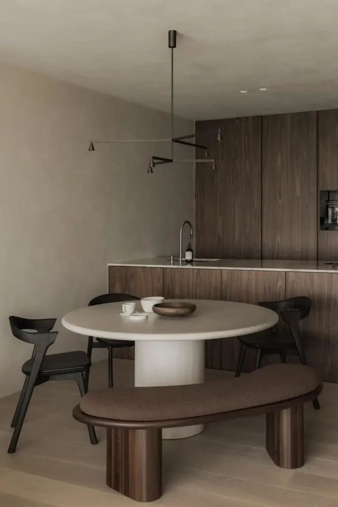 Ronde eettafel met zitbank en zwarte stoelen voor de houten keuken met hanglamp, Appartement in Nieuwpoort, interieur Laura Calleeuw