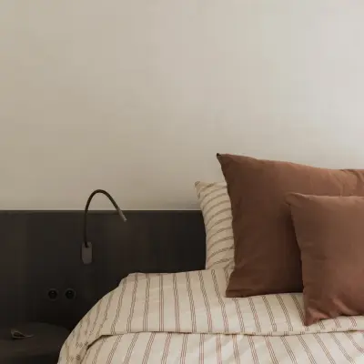 Donker hoofdbord met leeslamp en gestreept beddengoed, Appartement in Nieuwpoort, interieur Laura Calleeuw