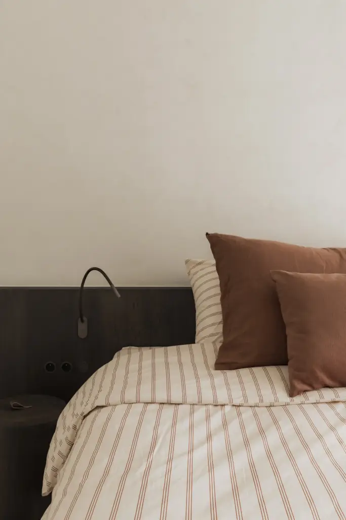 Donker hoofdbord met leeslamp en gestreept beddengoed, Appartement in Nieuwpoort, interieur Laura Calleeuw