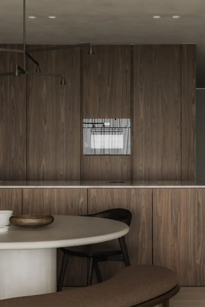 Houten keukenkasten met inbouwoven en een ronde eettafel op de voorgrond, Appartement in Nieuwpoort, interieur Laura Calleeuw