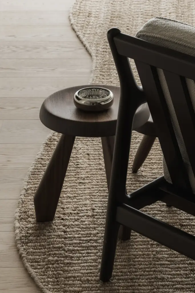 Houten kruk op een jute tapijt naast een houten fauteuil, Appartement in Nieuwpoort, interieur Laura Calleeuw