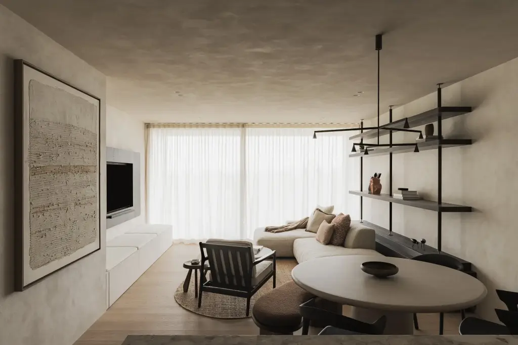 Zithoek met fauteuil, ronde salontafel en schilderij voor ramen met vitrage, Appartement in Nieuwpoort, interieur Laura Calleeuw