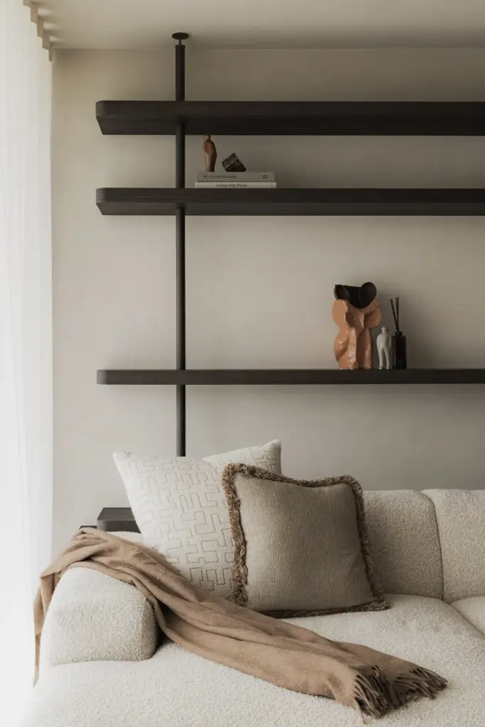 Planken met vazen en boeken boven een sofa met kussens, Appartement in Nieuwpoort, interieur Laura Calleeuw