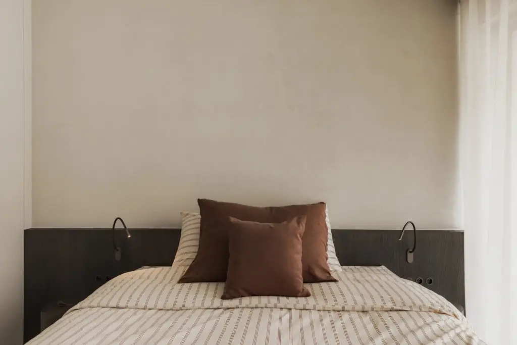 Slaapkamer met bed in gestreept beddengoed, terracotta kussens en donker hoofdbord, Appartement in Nieuwpoort, interieur Laura Calleeuw