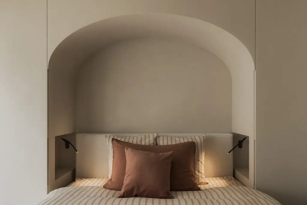Bed in een boogvormige gepleisterde nis met leeslampjes en terracotta kussens, Appartement in Nieuwpoort, interieur Laura Calleeuw