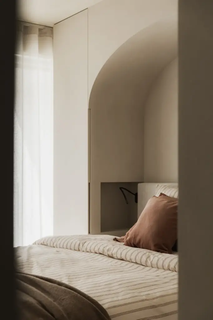 Slaapkamer met boogvormige nis, bed en spiegeling in de wand, Appartement in Nieuwpoort, interieur Laura Calleeuw