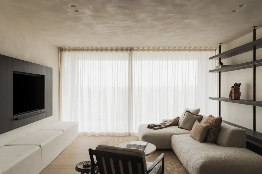 Zithoek met sofa, fauteuil en open rekken voor grote ramen met vitrage, Appartement in Nieuwpoort, interieur Laura Calleeuw