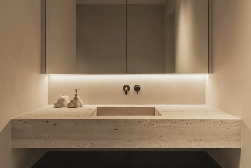 Badkamer met wastafel in travertijn, wandkranen en spiegelkasten met indirect licht, Gezinsvilla in Heusden-Zolder, interieur Laura Calleeuw