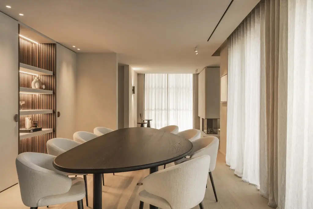 Eetkamer met ovale donkere tafel, ronde stoelen en een verlichte kast met ribbelwand, Gezinsvilla in Heusden-Zolder, interieur Laura Calleeuw