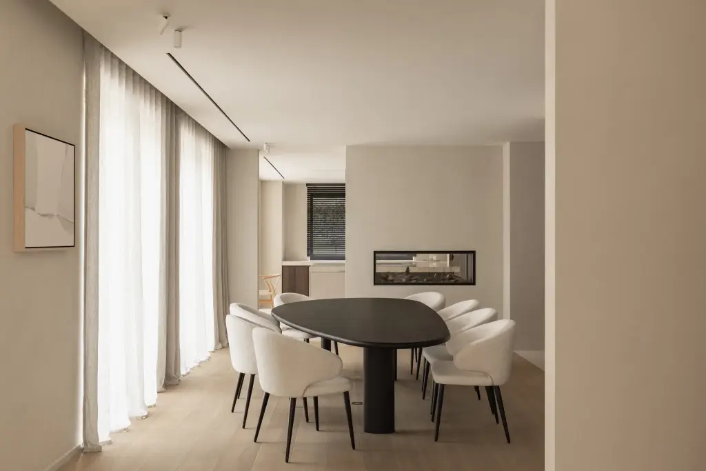 Eetkamer met ovale donkere tafel, ronde witte stoelen en een lage open haard, Gezinsvilla in Heusden-Zolder, interieur Laura Calleeuw