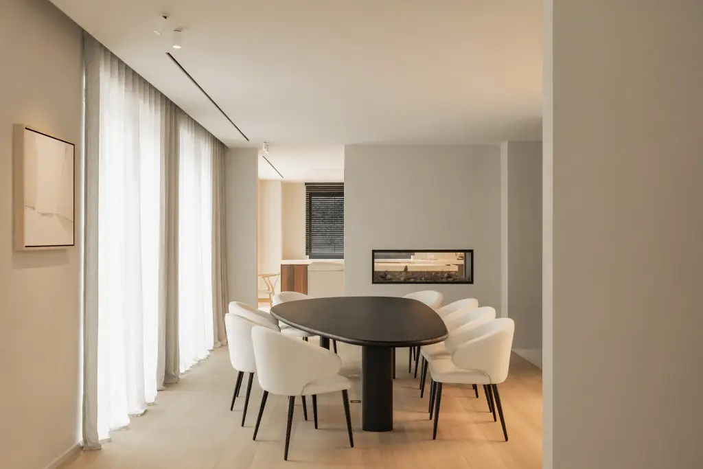 Eetkamer met ovale donkere tafel, ronde witte stoelen en een lage open haard, Gezinsvilla in Heusden-Zolder, interieur Laura Calleeuw