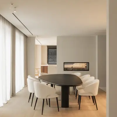 Eetkamer met ovale donkere tafel, ronde witte stoelen en een lage open haard, Gezinsvilla in Heusden-Zolder, interieur Laura Calleeuw