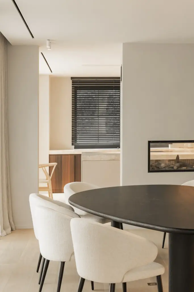 Ovale tafel met ronde witte stoelen en doorkijk naar de haard, Gezinsvilla in Heusden-Zolder, interieur Laura Calleeuw