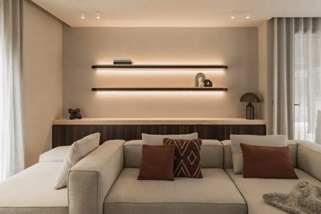 Hoeksofa met terracotta kussens voor een houten kast met verlichte wandplanken, Gezinsvilla in Heusden-Zolder, interieur Laura Calleeuw