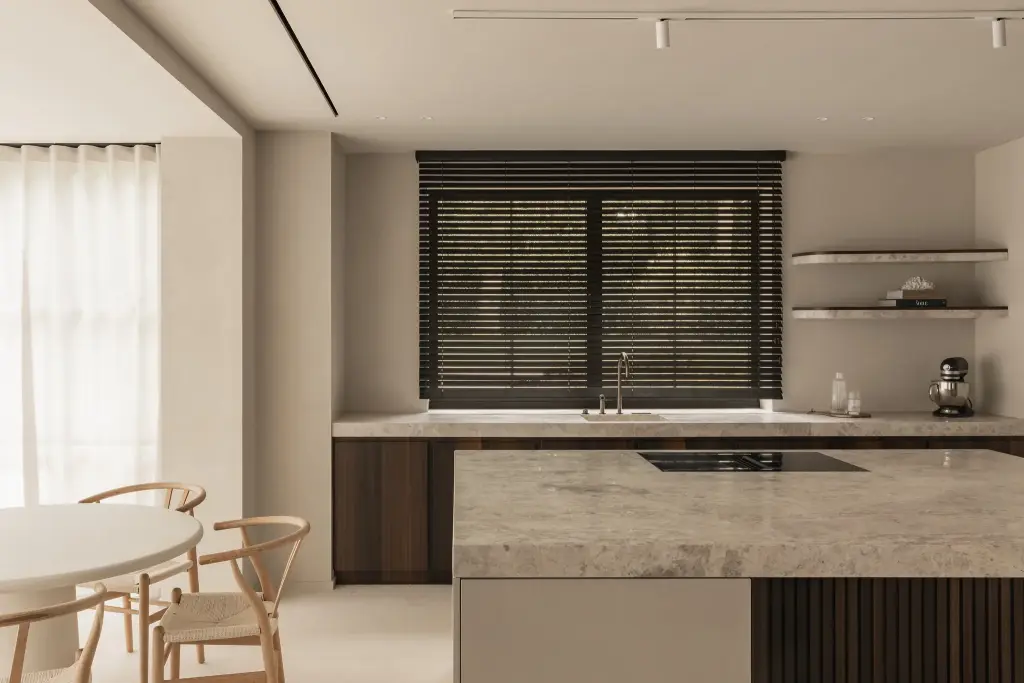 Keuken met kookeiland in natuursteen, jaloezieën, wandplanken en een eethoek met houten stoelen, Gezinsvilla in Heusden-Zolder, interieur Laura Calleeuw