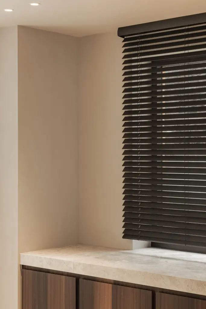 Hoek van de keuken met natuurstenen werkblad voor een raam met jaloezie, Gezinsvilla in Heusden-Zolder, interieur Laura Calleeuw