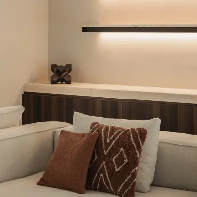 Sofa met terracotta kussens voor een houten kast met verlichte planken, Gezinsvilla in Heusden-Zolder, interieur Laura Calleeuw