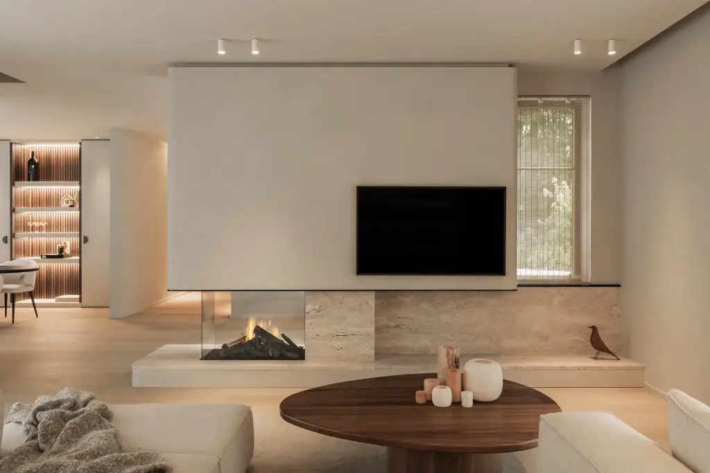 Leefruimte met televisie boven een open haard in natuursteen en een ovale houten salontafel, Gezinsvilla in Heusden-Zolder, interieur Laura Calleeuw