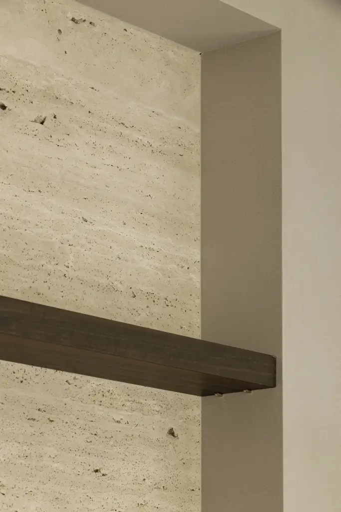 Detail van een travertijnen wand met donkere houten plank, Gezinsvilla in Heusden-Zolder, interieur Laura Calleeuw