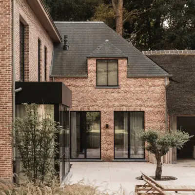 Gevel van de baksteenvilla met zwarte ramen en terras, Gezinsvilla in Heusden-Zolder, interieur Laura Calleeuw