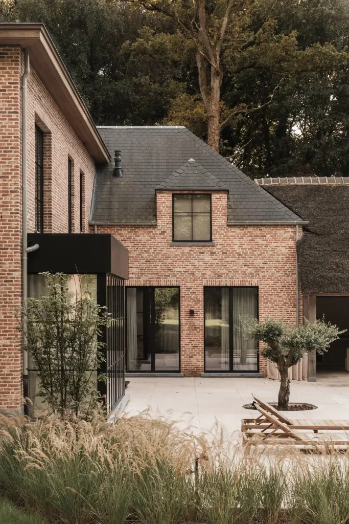 Gevel van de baksteenvilla met zwarte ramen en terras, Gezinsvilla in Heusden-Zolder, interieur Laura Calleeuw