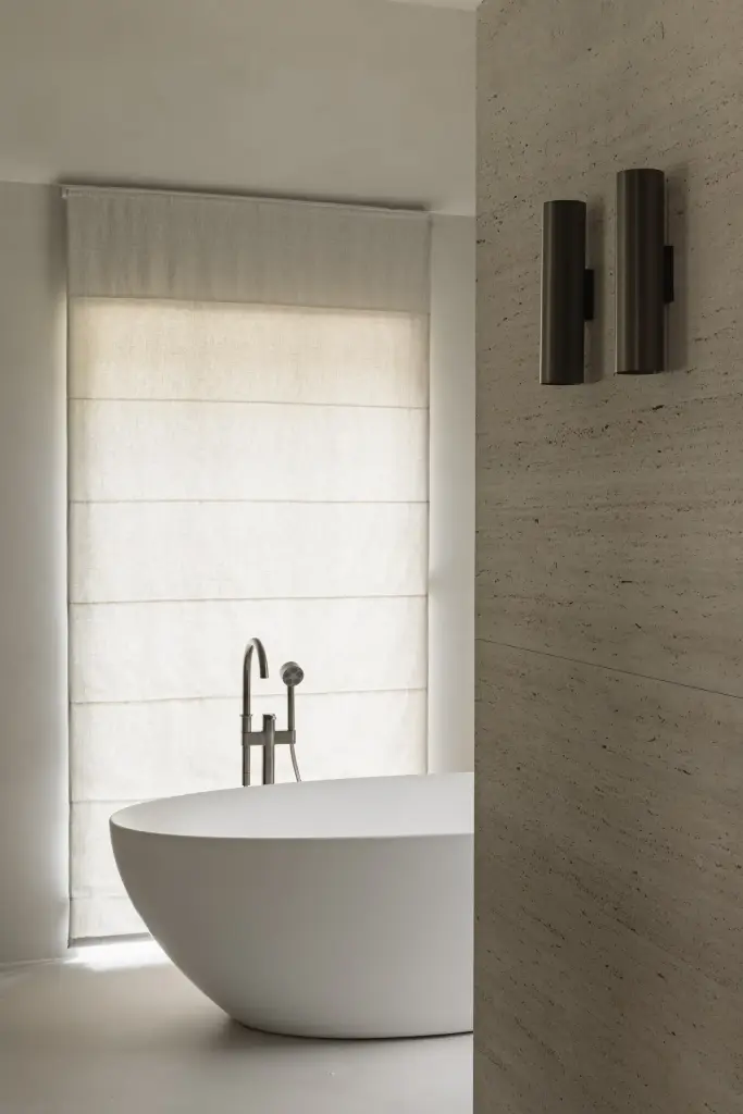 Vrijstaand bad met badkraan, wandlamp en roman blind bij het raam, Gezinsvilla in Heusden-Zolder, interieur Laura Calleeuw