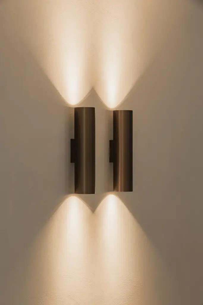 Bronzen wandlamp met licht naar boven en onder tegen een gepleisterde wand, Gezinsvilla in Heusden-Zolder, interieur Laura Calleeuw