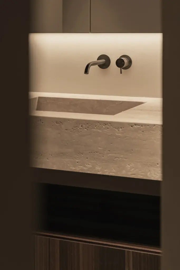 Travertijnen wastafel met wandkranen in een donkere nis, Gezinsvilla in Heusden-Zolder, interieur Laura Calleeuw