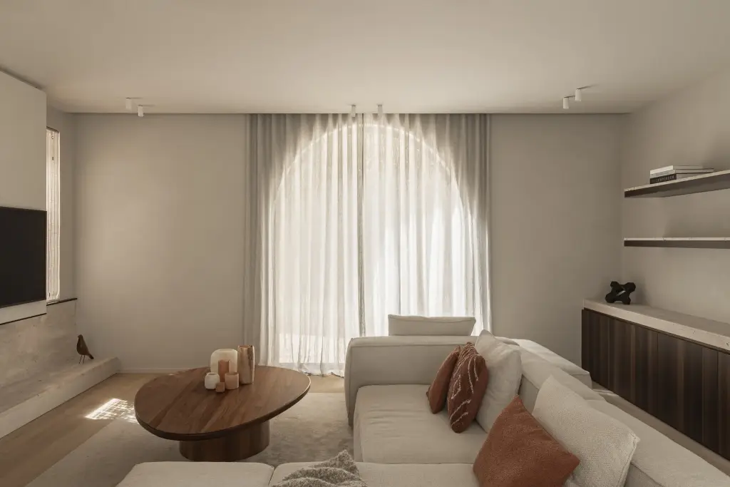 Zithoek met boogvormig raam, lage ovale salontafel in notelaar en hoeksofa, Gezinsvilla in Heusden-Zolder, interieur Laura Calleeuw