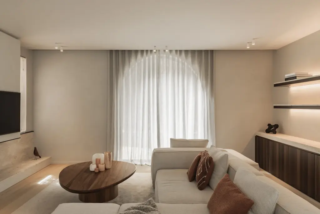 Zithoek met boogvormig raam, lage ovale salontafel in notelaar en hoeksofa, Gezinsvilla in Heusden-Zolder, interieur Laura Calleeuw