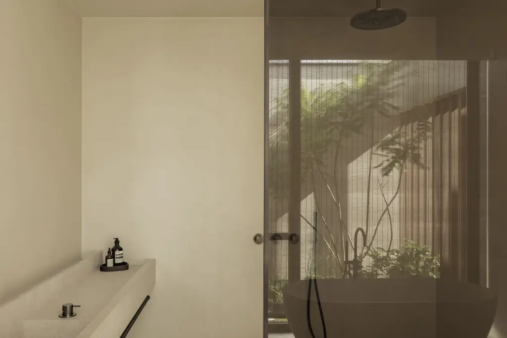 Badkamer met vrijstaand bad, regendouche achter glas en zicht op de patio, a home that invites you to slow down, interieur Laura Calleeuw