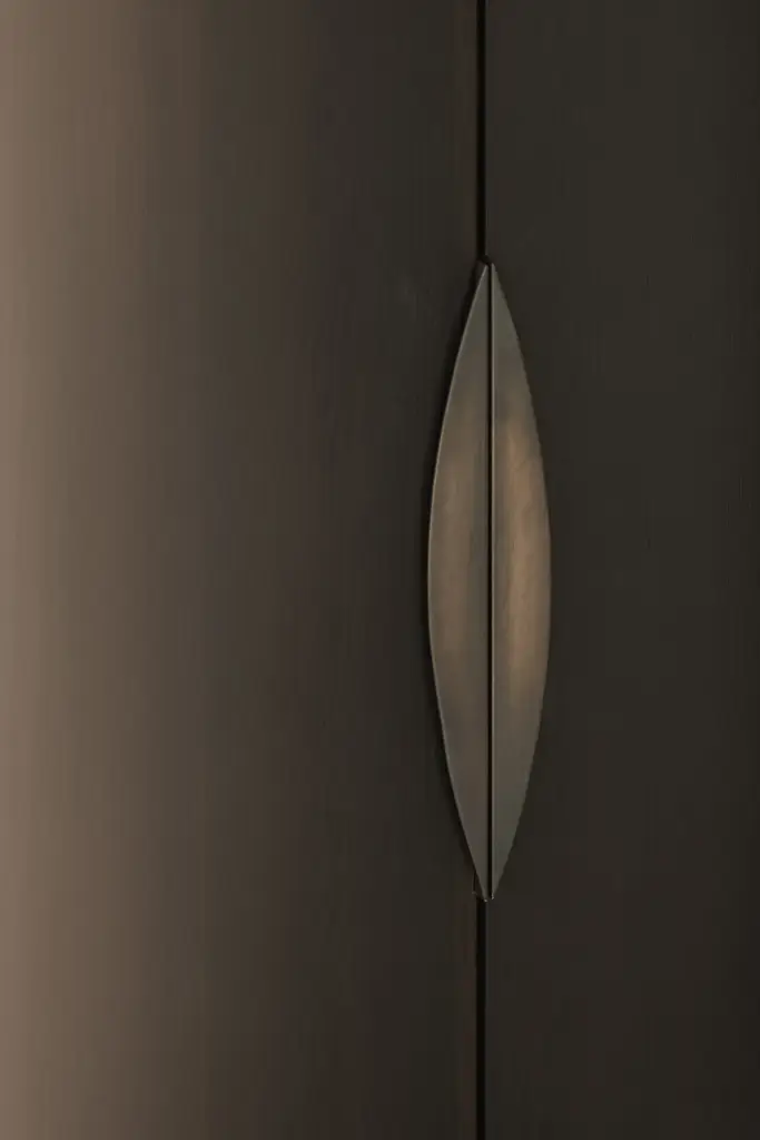 Detail van een bronzen gebogen greep op een donkere houten kastdeur, a home that invites you to slow down, interieur Laura Calleeuw