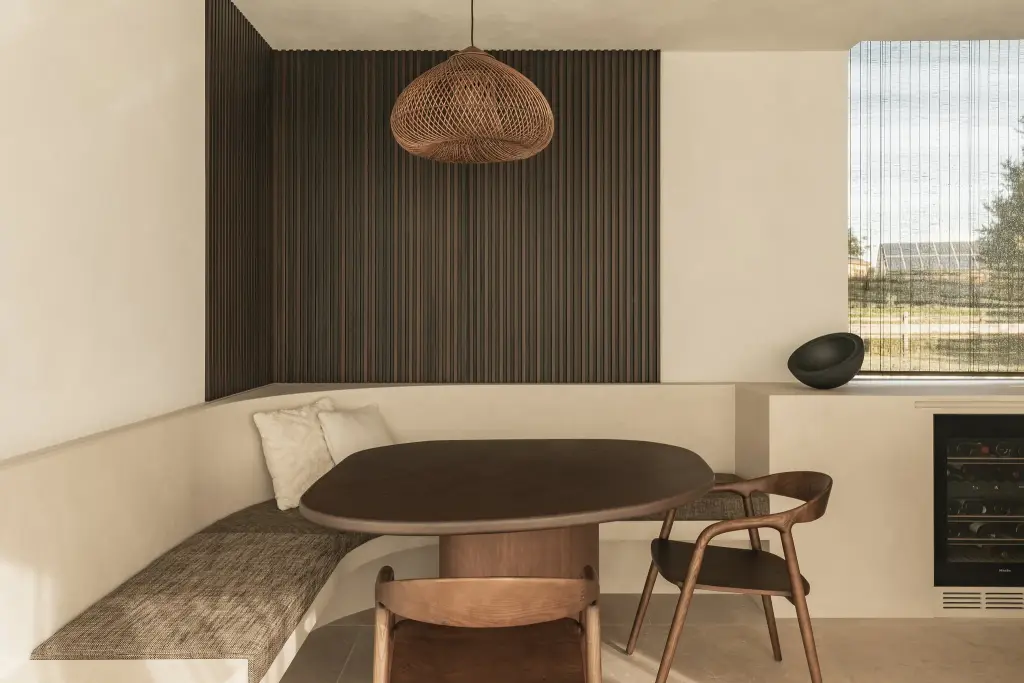 Eethoek met inbouwbank, ovale houten tafel, stoelen en een rotan hanglamp voor een houten ribbelwand, a home that invites you to slow down, interieur Laura Calleeuw