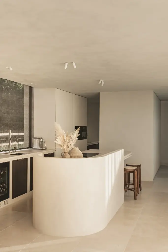 Open keuken met gebogen kookeiland in kalkpleister, pampasgras en houten krukken, a home that invites you to slow down, interieur Laura Calleeuw