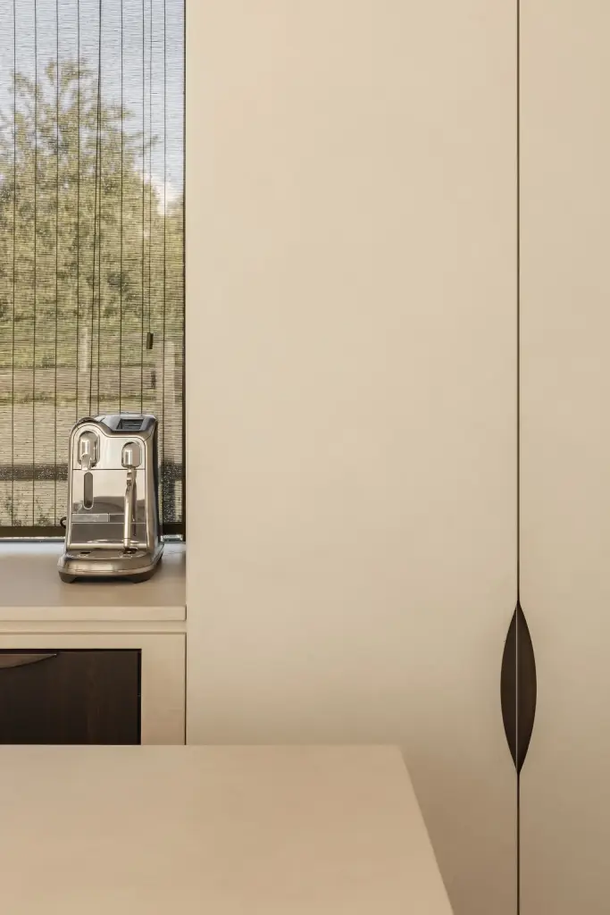 Koffiemachine naast een kastdeur met ingefreesde greep en een raam met rieten zonwering, a home that invites you to slow down, interieur Laura Calleeuw