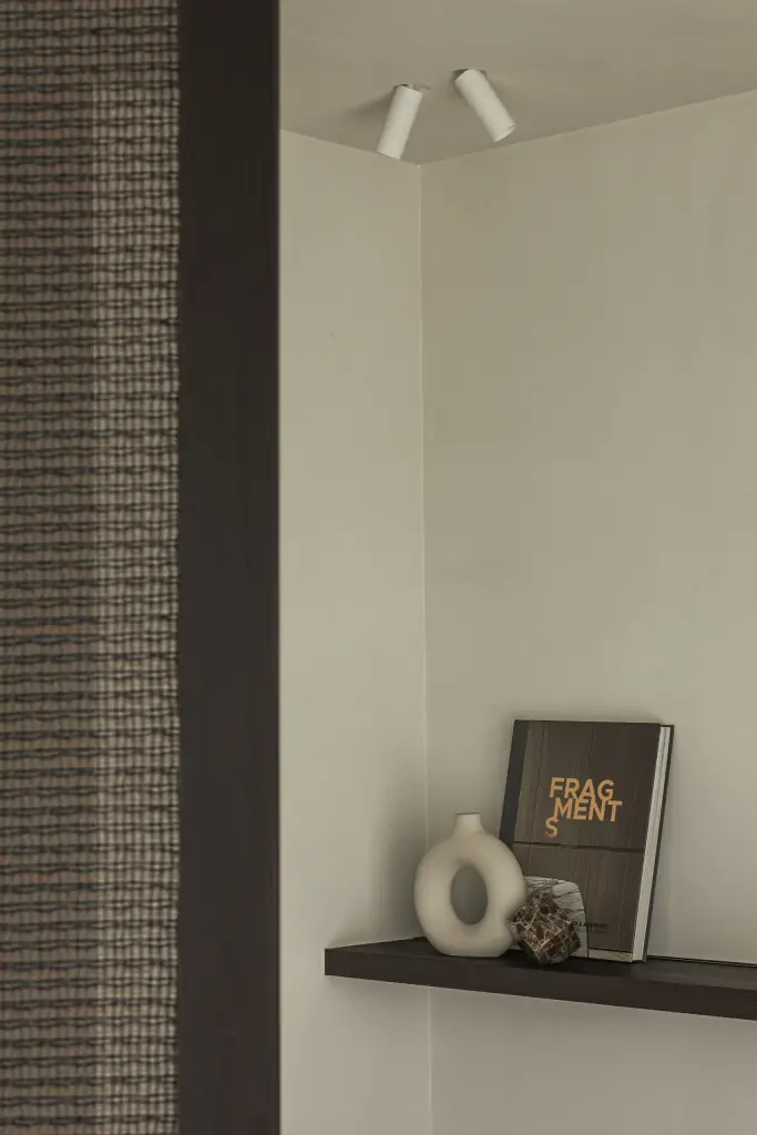 Plank met boek en vaas onder twee spots naast een geweven wand, a home that invites you to slow down, interieur Laura Calleeuw