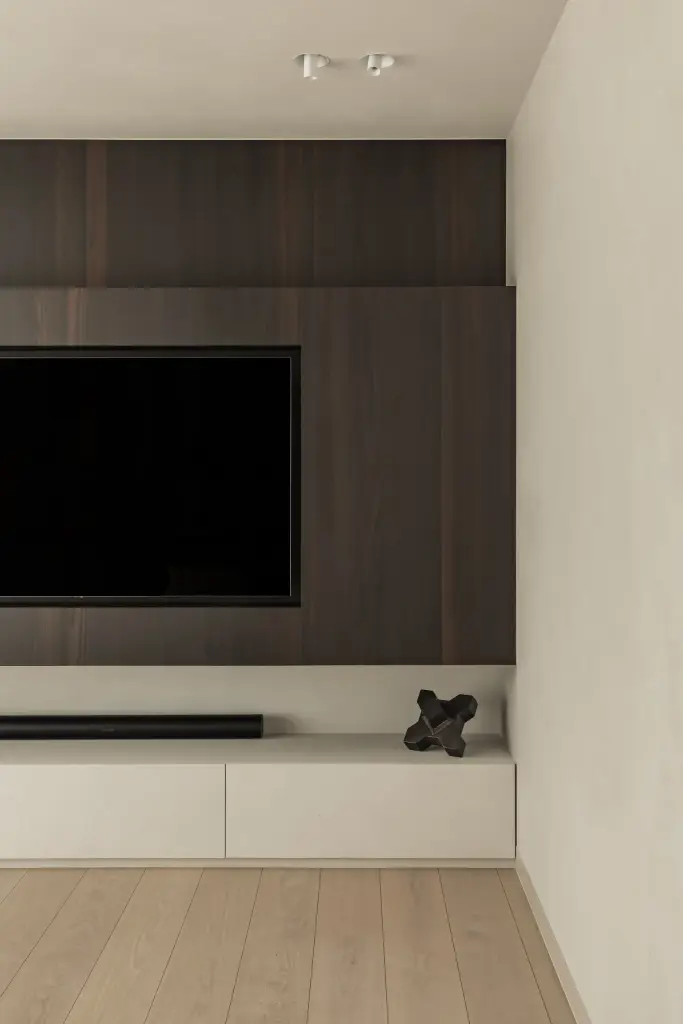Televisie in een donker houten paneel boven een laag wit meubel, a home that invites you to slow down, interieur Laura Calleeuw