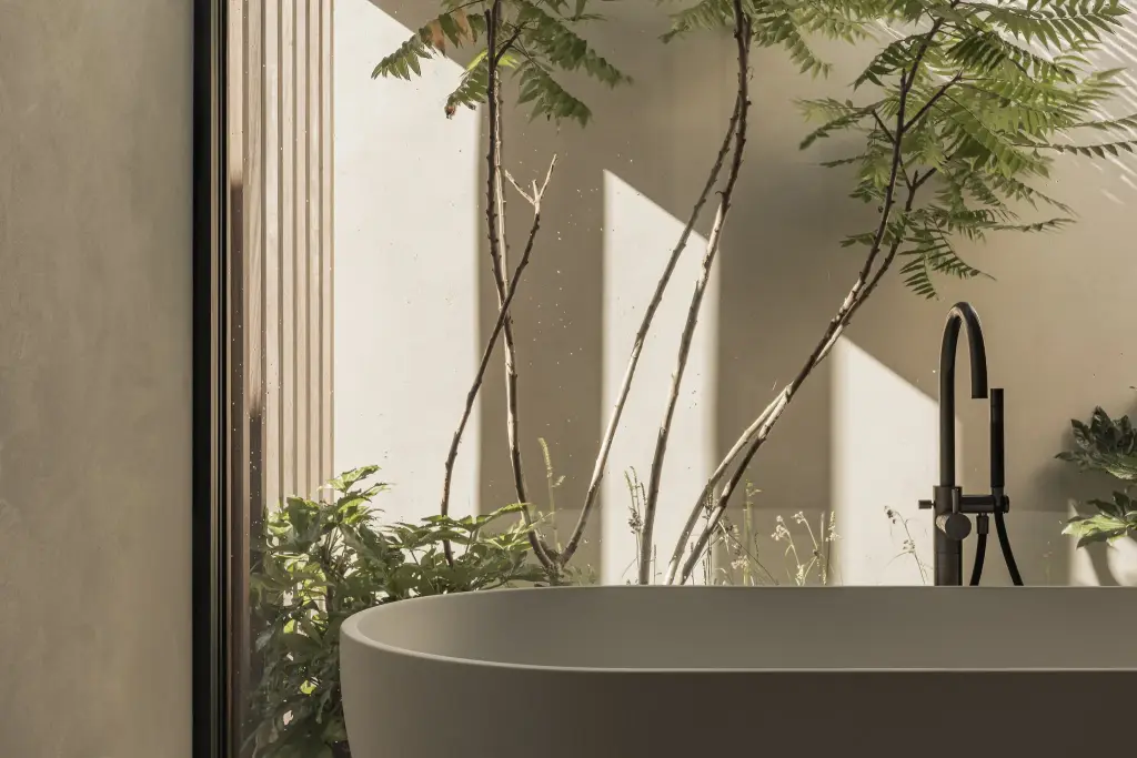 Vrijstaand bad met zwarte badkraan voor een glazen wand met patio en planten, a home that invites you to slow down, interieur Laura Calleeuw