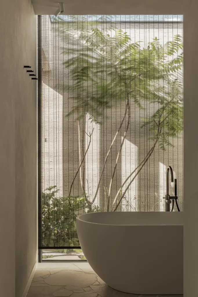 Vrijstaand bad bij een hoog venster met zicht op de boom in de patio, a home that invites you to slow down, interieur Laura Calleeuw