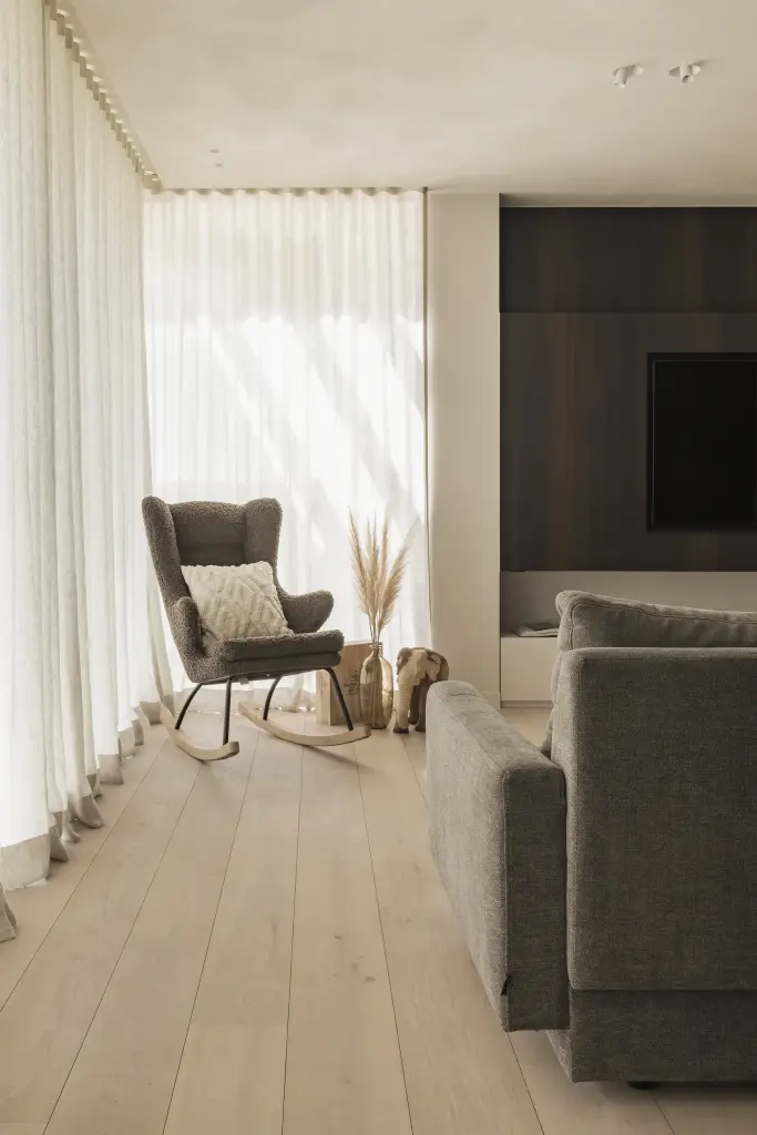 Zitkamer met schommelstoel, houten olifantjes, vitrage en een televisiepaneel in donker hout, a home that invites you to slow down, interieur Laura Calleeuw