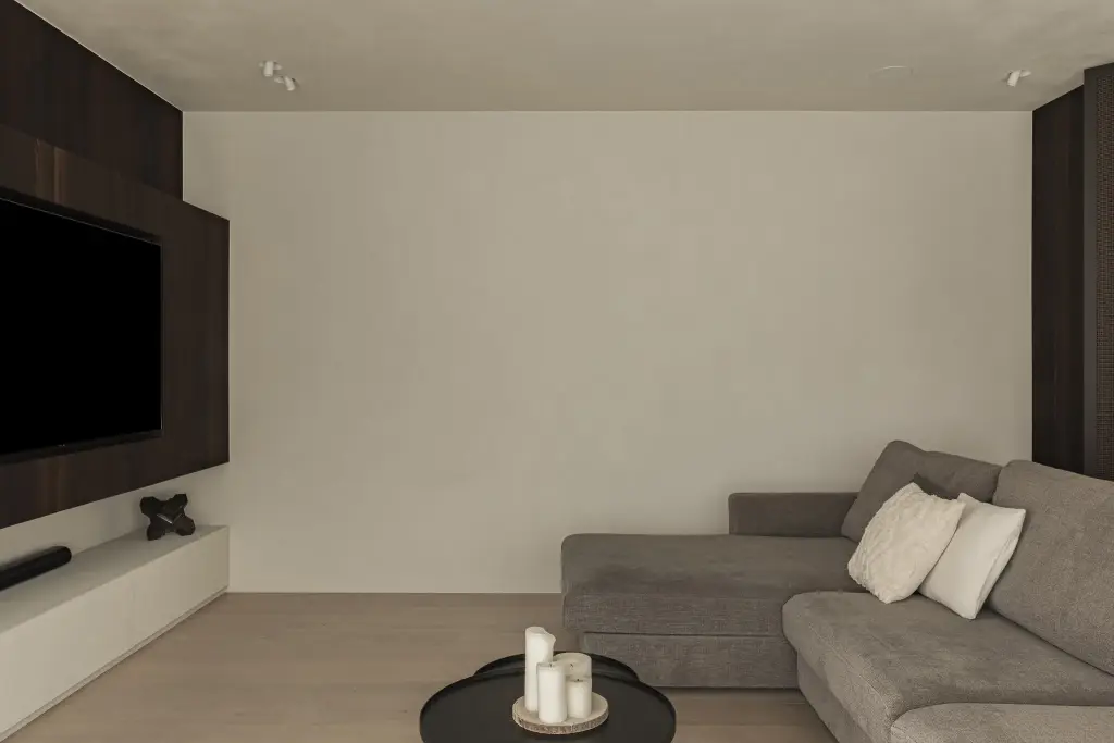 Zitkamer met televisiepaneel in donker hout, laag meubel, hoeksofa en zwarte salontafel, a home that invites you to slow down, interieur Laura Calleeuw