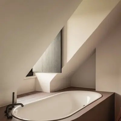Inbouwbad onder de dakhelling met bordeauxkleurige omkasting en zwarte badkraan, Hoeve in Westkapelle, interieur Laura Calleeuw