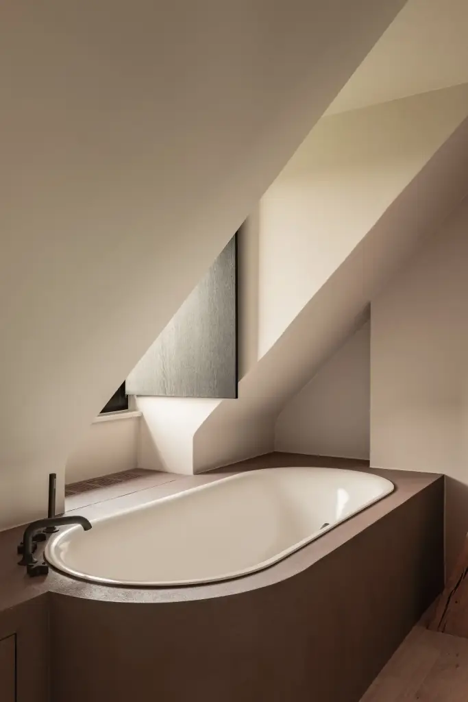 Inbouwbad onder de dakhelling met bordeauxkleurige omkasting en zwarte badkraan, Hoeve in Westkapelle, interieur Laura Calleeuw