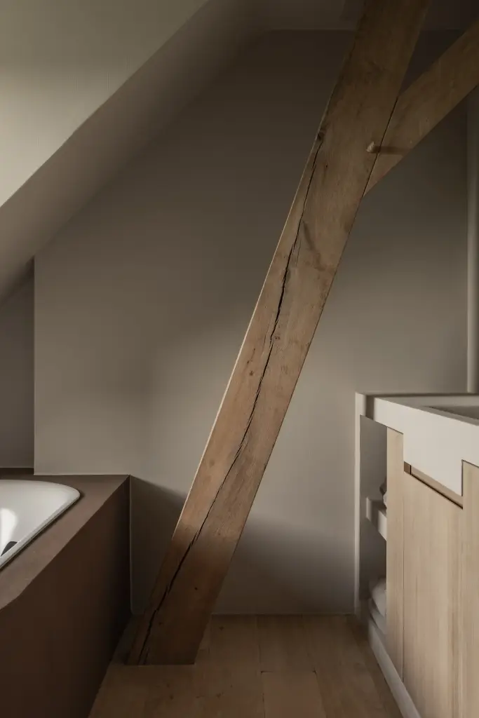 Badkamer onder de dakhelling met een zichtbare houten balk en inbouwbad, Hoeve in Westkapelle, interieur Laura Calleeuw