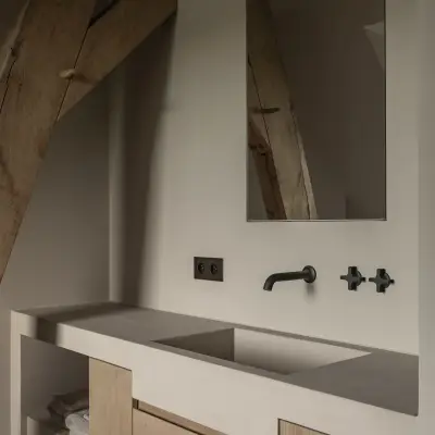 Badkamer met wastafel op eikenhouten onderkast, kruiskranen en spiegel naast een houten balk, Hoeve in Westkapelle, interieur Laura Calleeuw