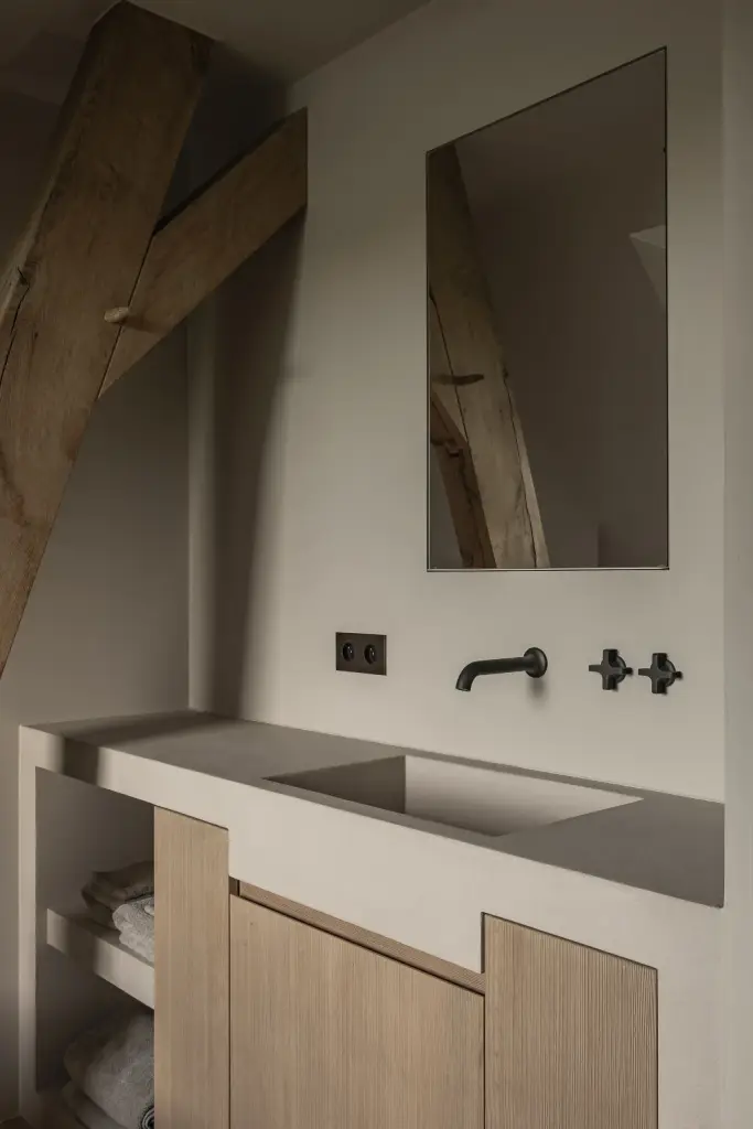 Badkamer met wastafel op eikenhouten onderkast, kruiskranen en spiegel naast een houten balk, Hoeve in Westkapelle, interieur Laura Calleeuw