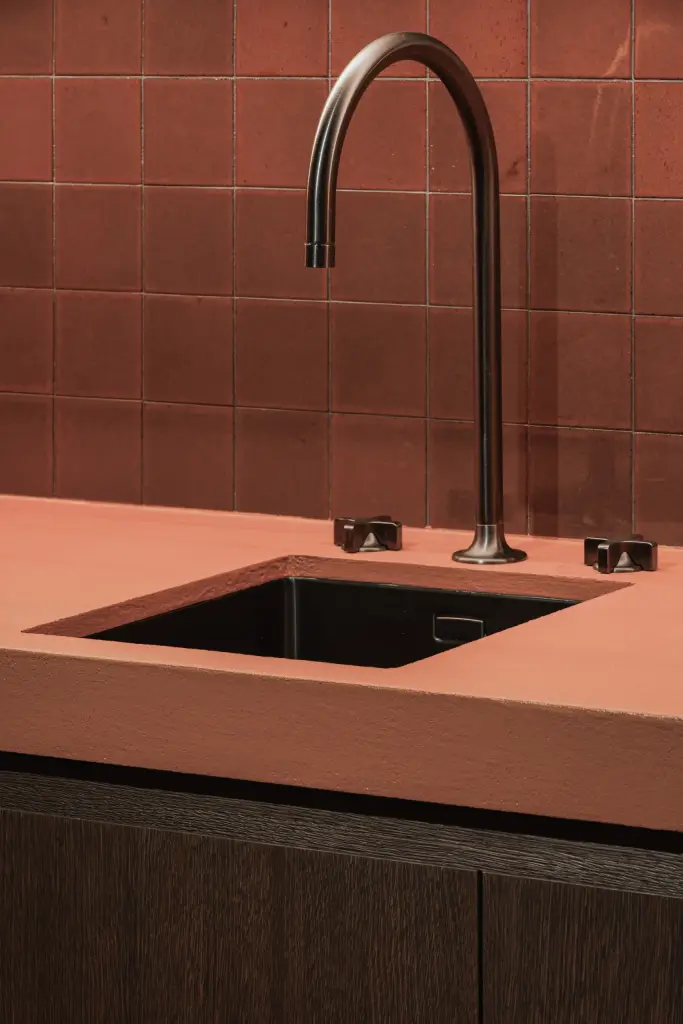 Spoelbak met zwarte kraan in een terracotta werkblad en tegelwerk, Hoeve in Westkapelle, interieur Laura Calleeuw